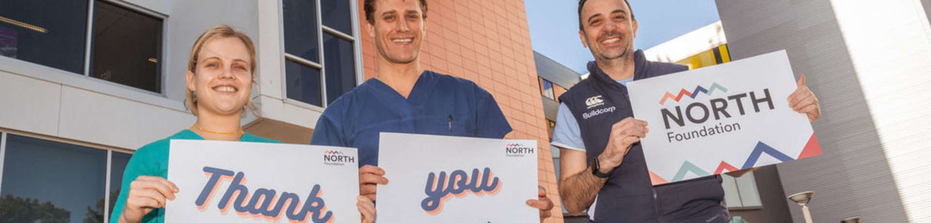A female and two male clinicians holding thank you signs