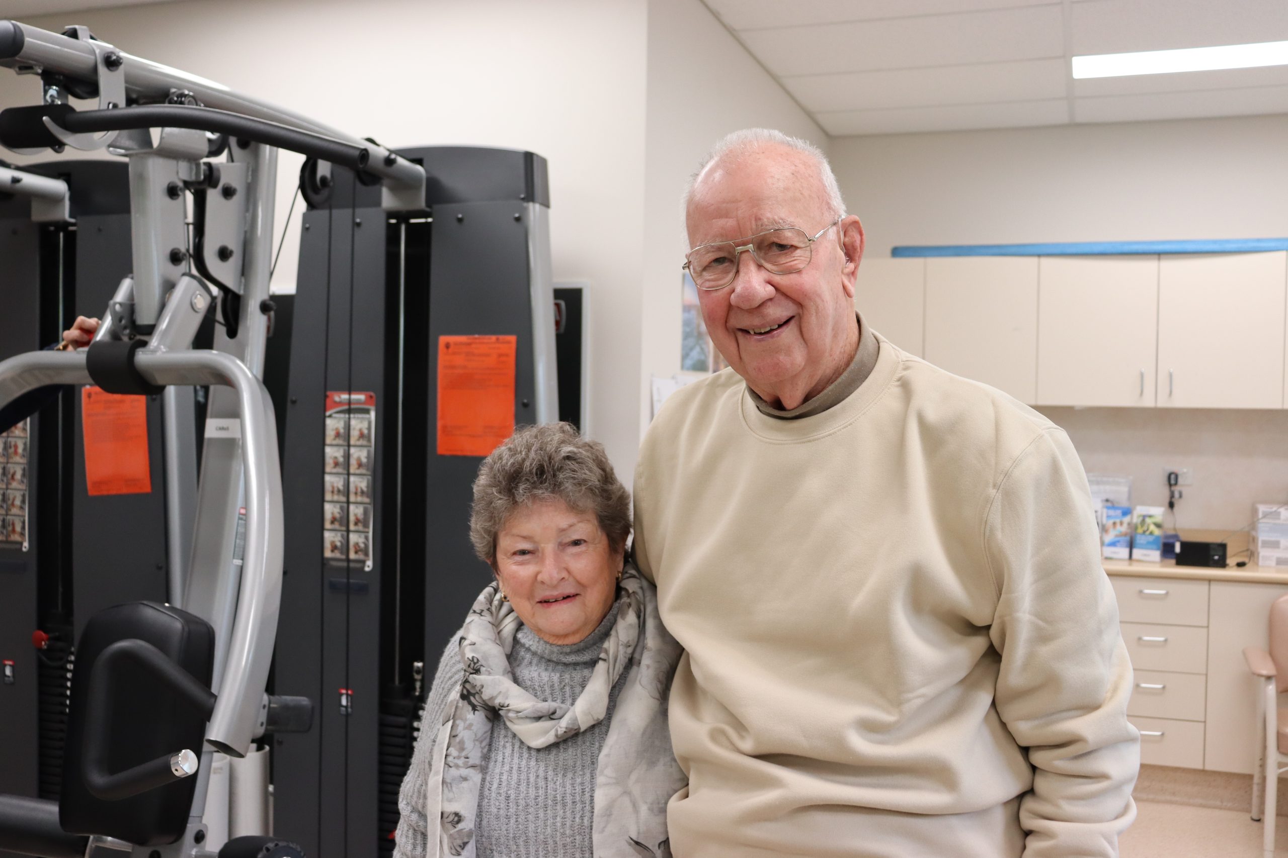 Husband and wife in their 80s smiling in a gym room