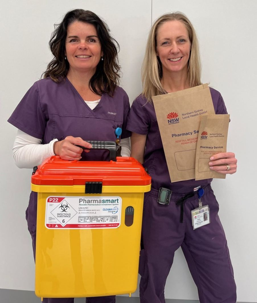 Two women holding up a paper bag and sharps bin