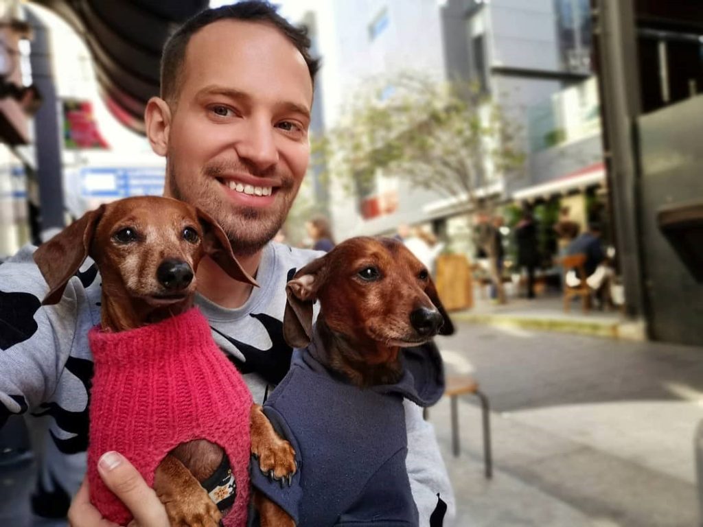 Young man smiling carrying his two small dachshund puppies