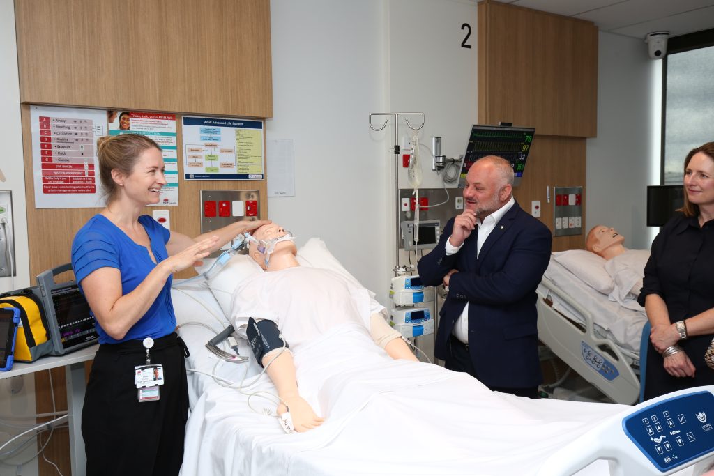 Man and woman standing over a dummy in a hospital bed