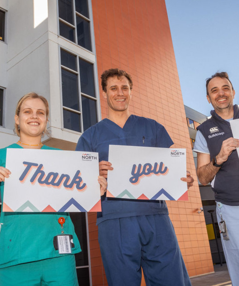 A female and two male clinicians holding thank you signs
